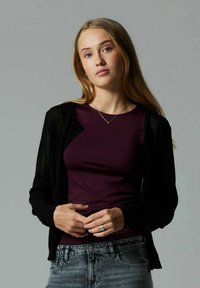 Black, lightweight, open-front cardigan over a fitted, dark purple top, paired with high-waisted, light gray denim jeans. Simple silver necklace accent.