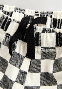 Pantalones cortos con cintura elástica de cuadros en blanco y negro y cordón negro atado en el centro delantero.