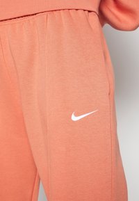 Nike sweatpants in soft, peach-colored fabric with an elastic waistband. Features a white logo on the side and a relaxed fit.