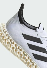 Scarpa sportiva bianca con una parte superiore testurizzata, accenti neri e un'inconfondibile suola intermedia a rete. Presenta tre strisce nere sul lato.