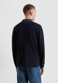 Marineblaues Langarm-Polohemd mit geripptem Kragen und weißen Streifen. Weicher Stoff mit lockerer Passform, kombiniert mit blauen Jeans.