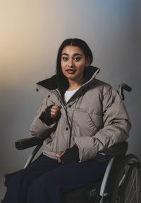 Light gray puffer jacket with a black collar and cuffs, featuring button closures and quilted texture, worn by a person in a wheelchair.