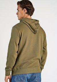 Olivgrön huvtröja i mjuk bomullsblandning, med dragsko på huvan, ribbade muddar och en avslappnad passform, kombinerad med blå denimjeans.