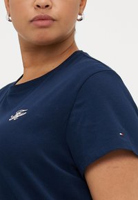 Marineblå bomulds t-shirt med rund halsudskæring, korte ærmer og et lille broderet logo på brystet. Accentueret med en farveblok på ærmet.