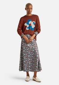 Brauner Strickpullover mit blau-weißen Blumenmuster, kombiniert mit einem braunen Maxirock mit floralen Mustern und beigen Loafers.