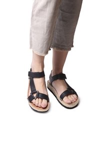 Black strappy sandals with textured straps, a wide ankle band, and woven natural fiber soles; rubber accents on the underside for grip.