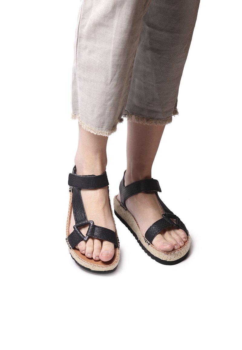 Black strappy sandals with textured straps, a wide ankle band, and woven natural fiber soles; rubber accents on the underside for grip.