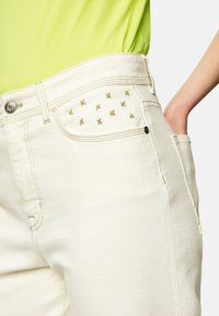 White denim jeans featuring subtle gold embroidered accents near the pocket, with a straight cut and standard waistband.