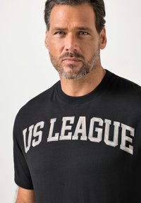 Czarny bawełniany T-shirt z dużym, jasnoszarym napisem „US LEAGUE” na przodzie, okrągłym dekoltem i krótkimi rękawami.