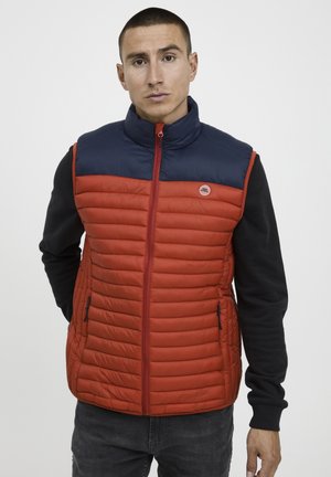 Chaleco acolchado en rojo y azul marino con un cuello alto, cremallera frontal y bolsillos laterales. Diseñado con una textura acolchada y colores contrastantes.