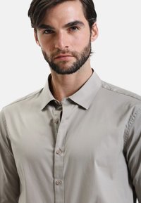 Camicia grigia chiaro con colletto a punta, tessuto liscio e morbido al tatto. Presenta una vestibilità slim e dettagli di cucitura discreti.