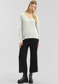 Lichtgrijze v-hals trui met ribbelstructuur aan de onderkant, gecombineerd met zwarte wijde broek en stevige zwarte laarzen, wat zorgt voor een casual outfit.