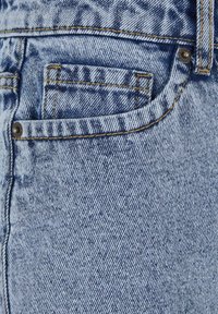 Light blue denim fabric with a close-up of a front pocket, showing orange stitching, rivets, and fabric texture.
