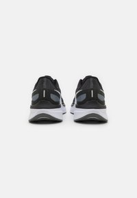 Scarpe da ginnastica nere e grigie con una tomaia in rete, dettagli riflettenti, suola ammortizzata e un design curvo distintivo, viste da dietro.