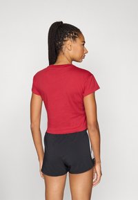 Κόκκινη κοντή μπλούζα με κοντά μανίκια, συνδυασμένη με μαύρο σορτς. Το ύφασμα φαίνεται λείο, με απλό σχέδιο και χωρίς ορατά μοτίβα.