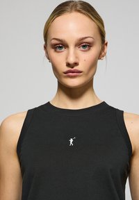 Czarna bezrękawnik z bawełny, z małym białym logo przedstawiającym osobę grającą w golfa na klatce piersiowej, okrągłym dekoltem i gładką fakturą.