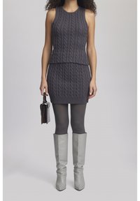 Harmaa neulekahden osan asu, johon kuuluu hihaton paita ja tiukka hame, jossa on kaapelikuosi. Yhdistetty harmaisiin leggingseihin ja polvimittaisiin saappaisiin.