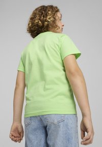 Zeleni bombažni T-shirt s kratkimi rokavi, okroglo izrezom in gladko teksturo; oblečen z svetlo modrimi kavbojkami.