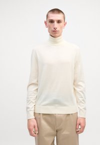 Pull à col roulé crème en tissu doux et léger ; poignets et ourlet côtelés ; silhouette ajustée avec un minimum de détails.