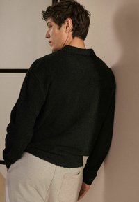 Sort tekstureret sweater med rund hals, afslappet pasform og lange ærmer, parret med lys grå sweatpants. Enkel design og dæmpede farver.