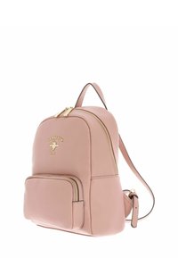 Sac à dos en cuir rose clair avec ferrures dorées, double fermeture éclair, logo embossé, poche avant et bretelles réglables. Texture lisse.