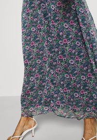 Floral maxi-jurk met een donkerblauwe achtergrond en roze en groene bloemen, gemaakt van lichtgewicht stof met een vloeiende uitstraling.
