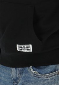 Black hoodie featuring a front pocket, with a white label reading "Original Denim Factory." Paired with light blue distressed denim.