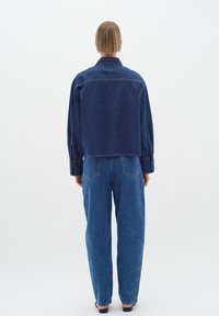 Denim jacket with a cropped back, dark blue color, and long sleeves; paired with loose-fitting dark blue jeans and black footwear.