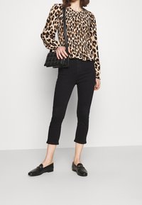 Blusa de leopardo con mangas largas, jeans negros cortos y mocasines negros planos. La modelo lleva un pequeño bolso de mano negro acolchado.