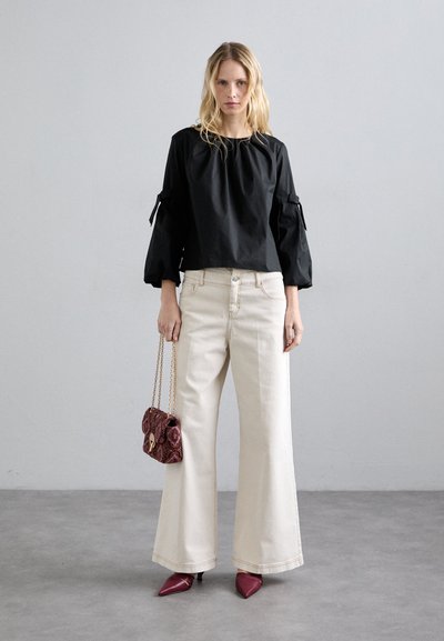 Čierna bavlnená blúzka s nadýchanými rukávmi, krémové široké nohavice a bordový kabelka s retiazkou. Model má na sebe bordové lodičky.