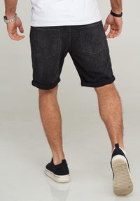 Mustat farkkushortsit, joissa on käännetyt lahkeet, kaksi takataskua ja tekstuuri, yhdistettynä mustiin lenkkareihin valkoisella pinnalla.