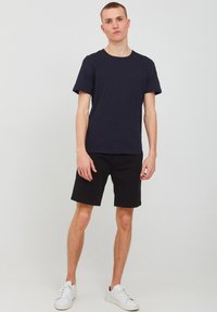 Tricou cu guler rotund din bumbac, asociat cu pantaloni scurți negri. Modelul poartă adidași albi. Design minimalist, mâneci scurte și fără modele.