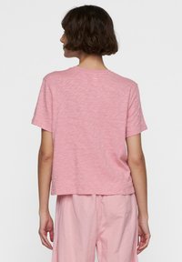Lyserød kortærmet t-shirt med tekstureret finish, rund hals og afslappet pasform, vist fra ryggen med matchende lyserøde underdele.