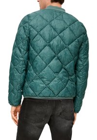 Türkise gesteppte Jacke mit Diamantmuster, weicher Textur und geripptem Kragen. Getragen mit schwarzen Jeans, zeigt Rückansicht und Ärmel.