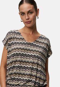Kortærmet top med et multikolor zigzag-mønster i beige, sort og grøn, med V-hals og blød tekstur.