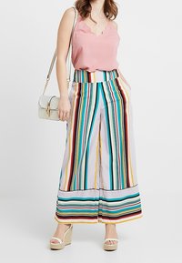 Pink scalloped tank top paired with wide-leg striped pants featuring vibrant colors. Accessories include a white bag and wedge sandals.
