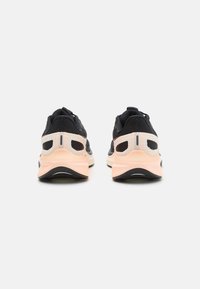 Baskets de sport noires et pêches avec une tige en maille texturée, une semelle rembourrée et un design de talon distinct avec des découpes.