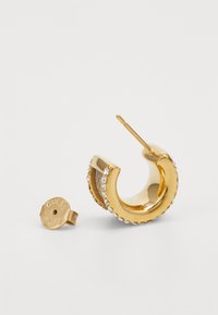 Golden hoop earring with a smooth surface, accented by small crystals and a textured edge. Includes a metal backing marked "GUESS."