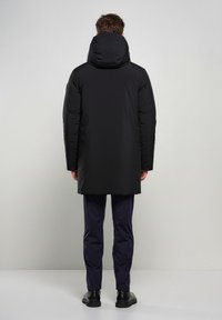 Sort polstret frakke med en stor hætte, designet med en lige pasform, og parret med marineblå bukser og sorte sko. Enkel og funktionel design.