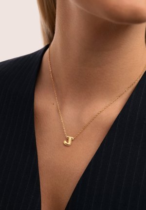 Gouden ketting met een gouden hanger in de vorm van de letter "J", gedragen om de nek van een persoon die een zwart gestreepte kleding draagt.
