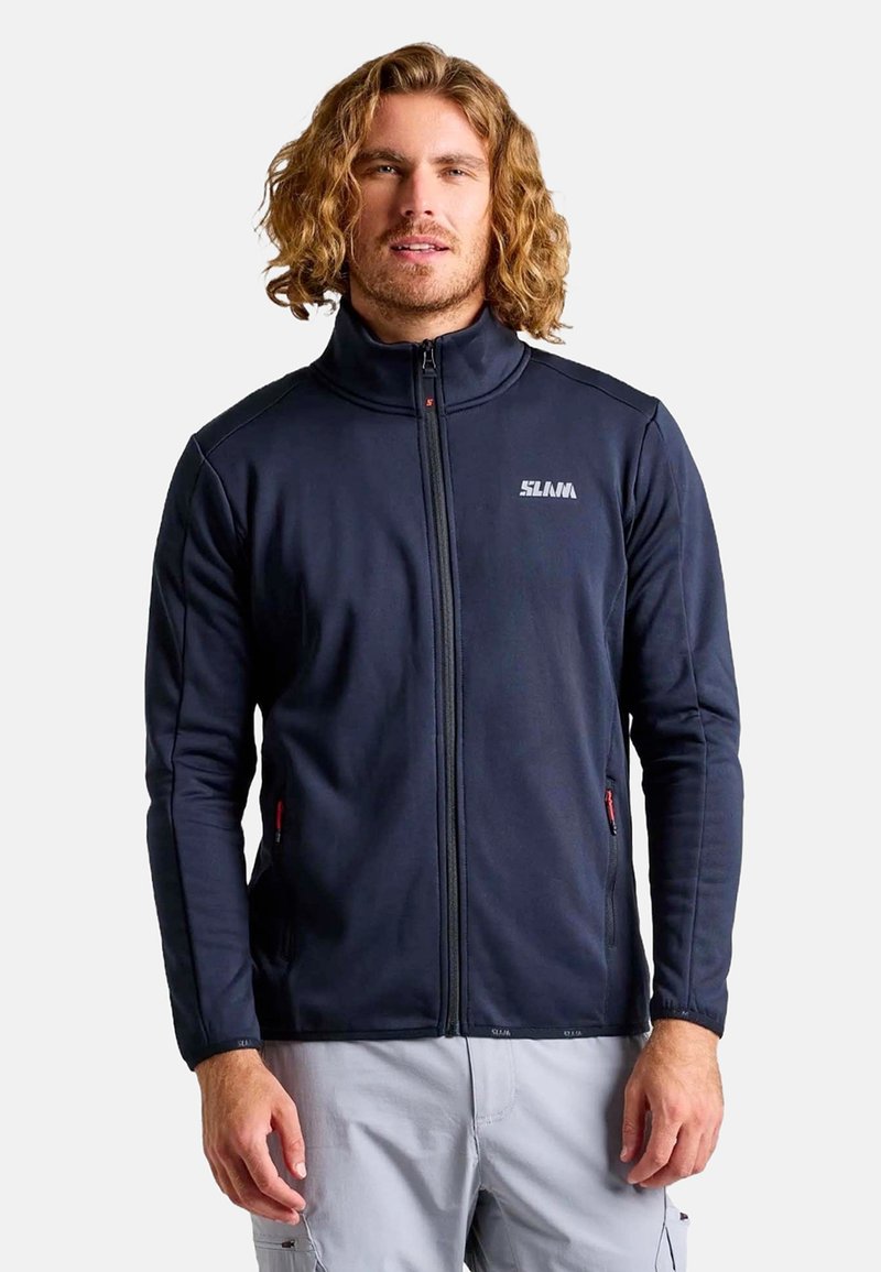 Veste zippée marine avec col montant, tissu texturé, poches latérales avec accents rouges et un logo sur la poitrine. Design lisse et ajusté.