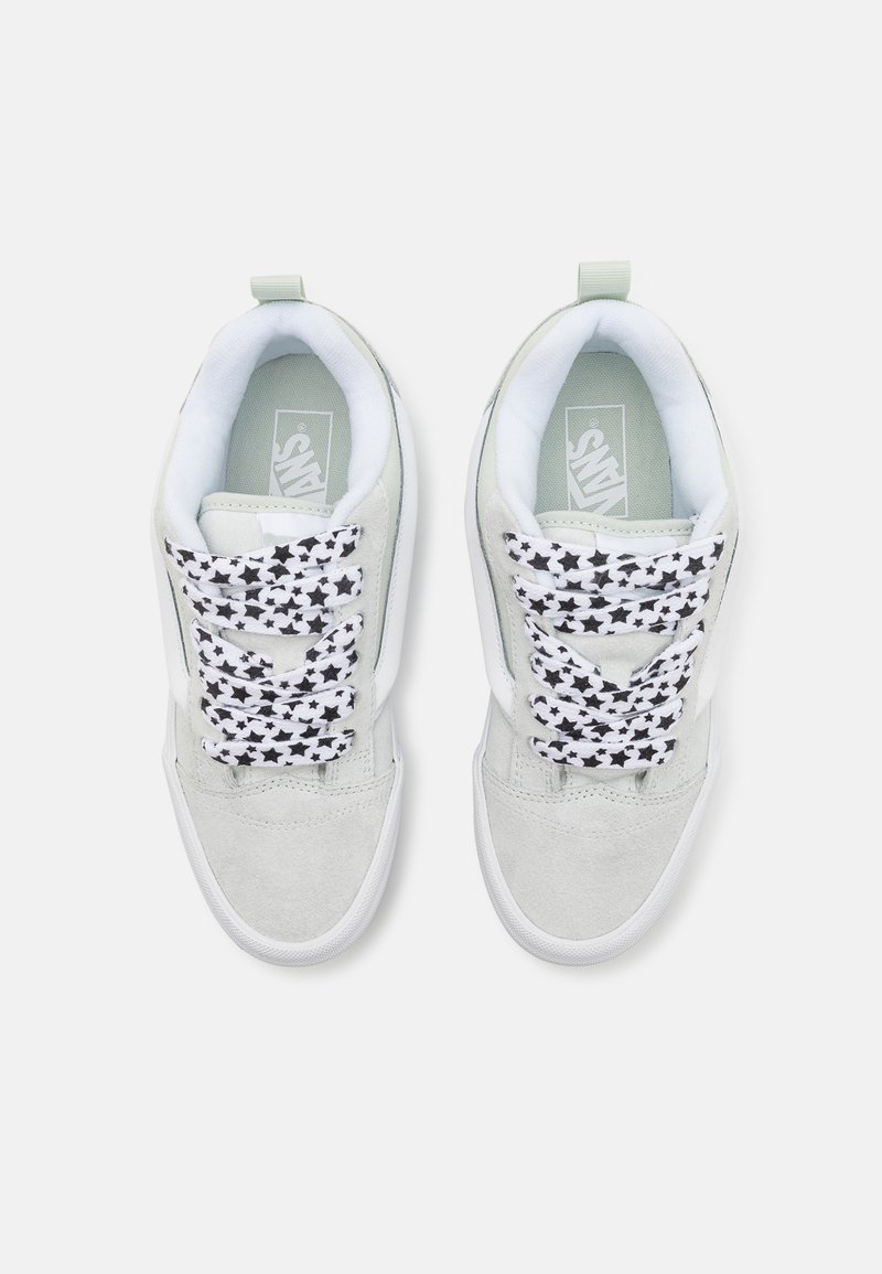 Zapatillas de ante gris claro con suelas de goma blancas, que cuentan con cordones con patrón de estrellas en blanco y negro y un cuello acolchado.