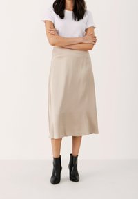 Beżowa satynowa spódnica midi o gładkiej teksturze i płynnej sylwetce, zestawiona z dopasowanymi czarnymi botkami za kostkę i białym t-shirtem.