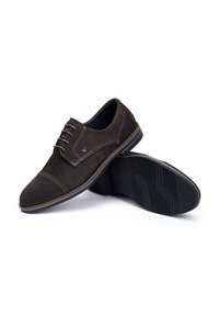 Zapatos de ante marrón con cordones y punta redonda, con costuras en contraste, que cuentan con una suela de goma texturizada y un sutil emblema de la marca.