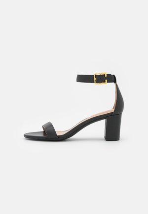 Sort læder open-toe sandal med en bred frontstropp, justerbar ankelrem og en solid blokkede hæl. Detalje med guldtonet spænde.