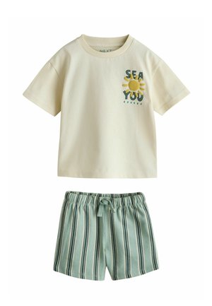 T-shirt beige à manches courtes avec l'inscription « SEA YOU » et un motif soleil, associé à un short taille élastique rayé verticalement vert et blanc.