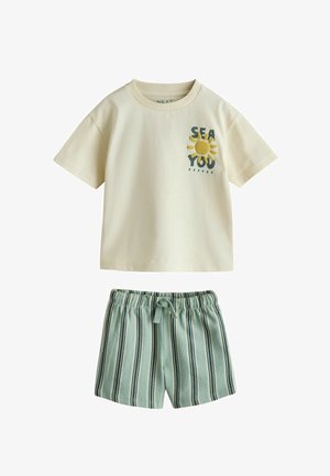 Bézs rövid ujjú póló "SEA YOU" felirattal és nap grafikával, zöld-fehér függőlegesen csíkos, elasztikus derékrészű rövidnadrággal kombinálva.