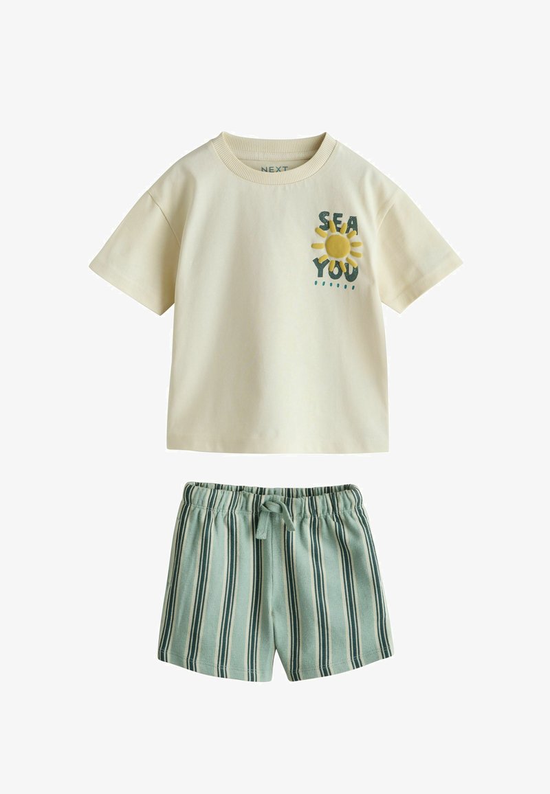 T-shirt beige à manches courtes avec l'inscription « SEA YOU » et un motif soleil, associé à un short taille élastique rayé verticalement vert et blanc.