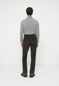 Chemise grise à manches longues associée à un pantalon en velours côtelé marron foncé. La tenue présente une texture lisse et un design ajusté.