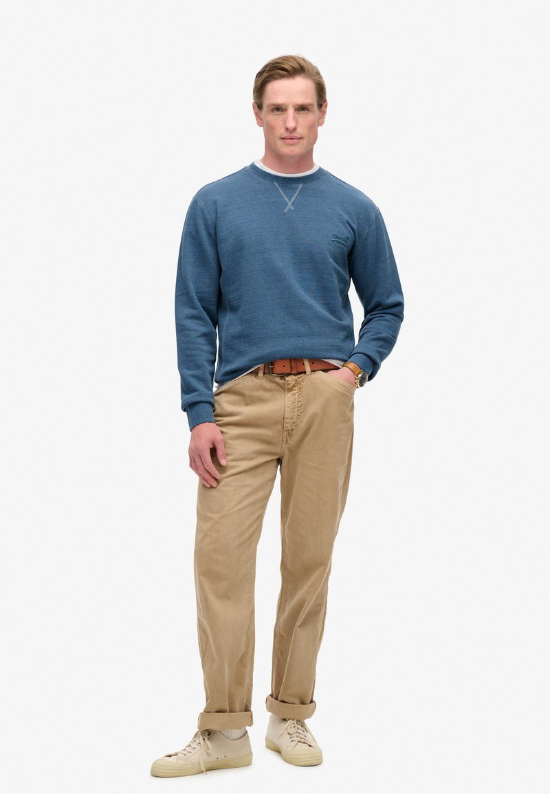 Sudadera azul con tejido texturizado, ribete crema en el escote, combinada con pantalones beige y zapatillas de color claro. Diseño sencillo, sin patrones.